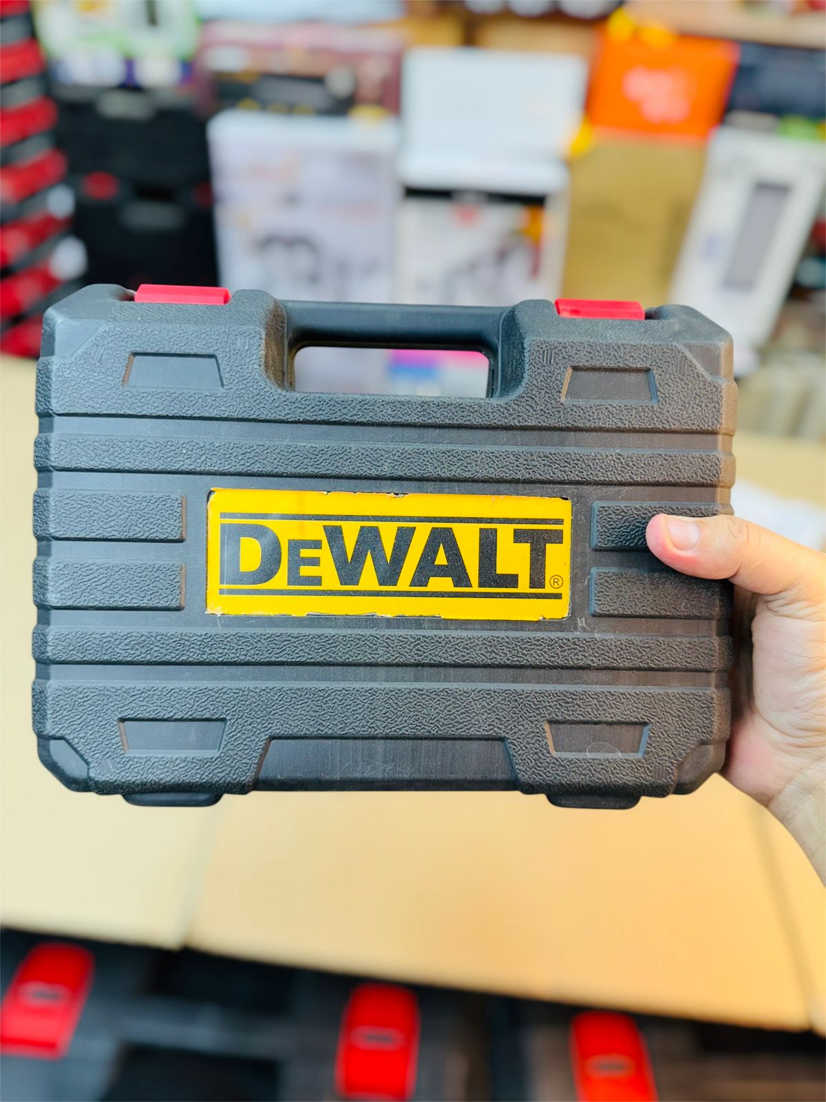 Black tool case with Dewalt logo held by a person in a blurred indoor setting