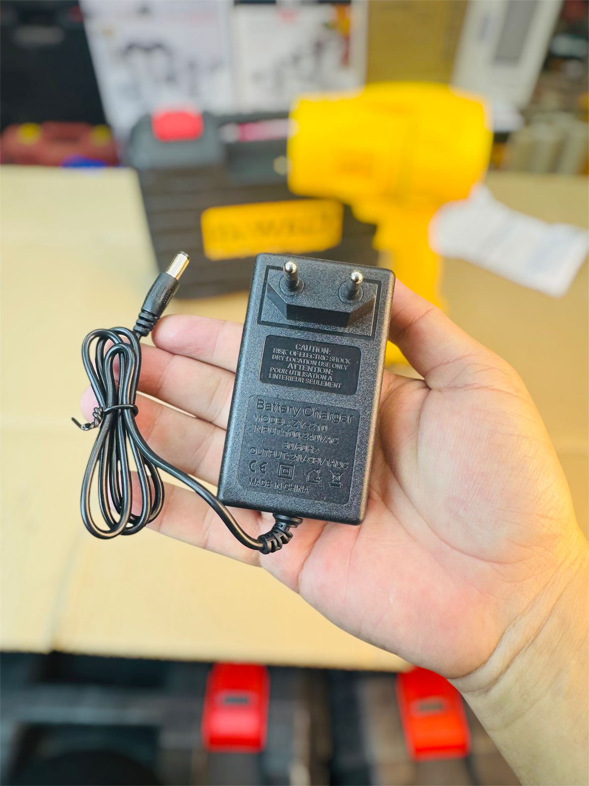 Hand holding a small black power adapter with a cable on a blurred background